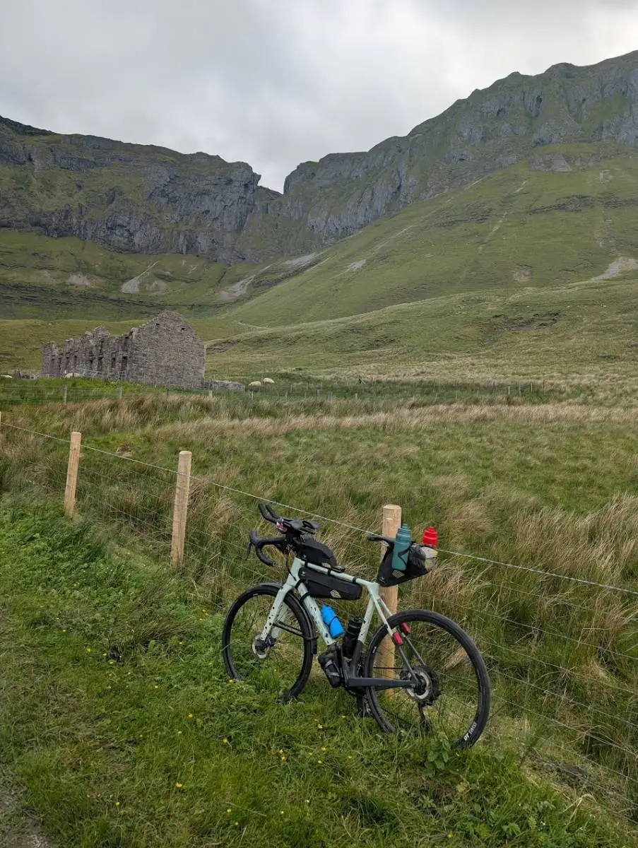 A bike against a fence below the cliffs of the Glenniff Horseshoe