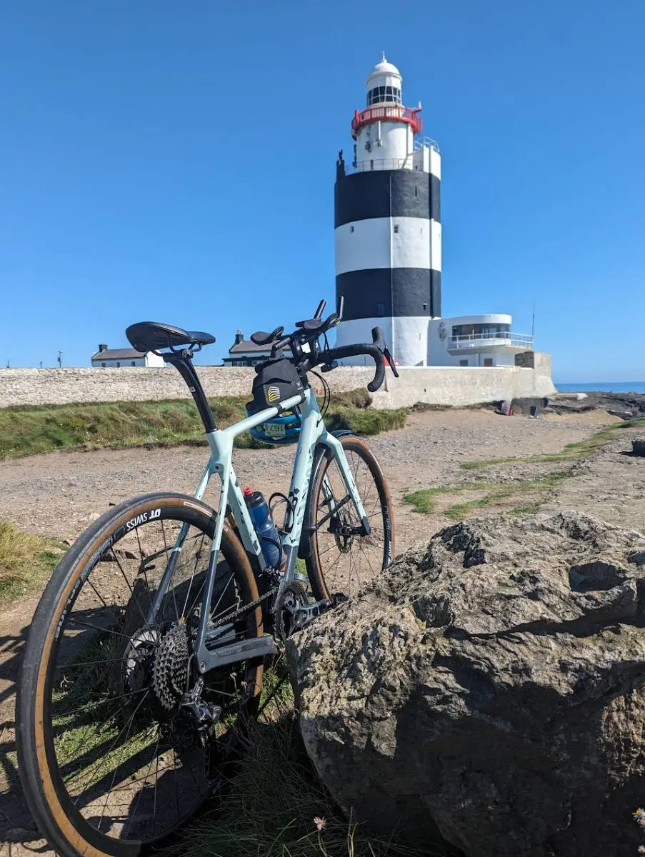 A bike leaning on a rock in front of the black and white Hook Head lighthouse