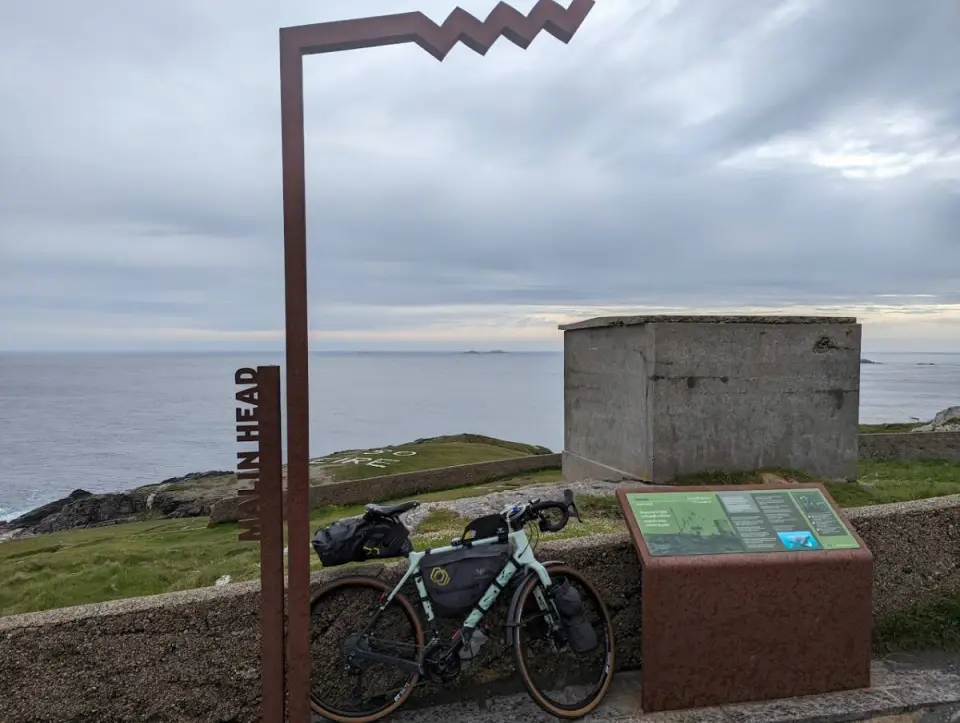 A loaded bike against a wall beside the Malin Head sign, with the sea behind