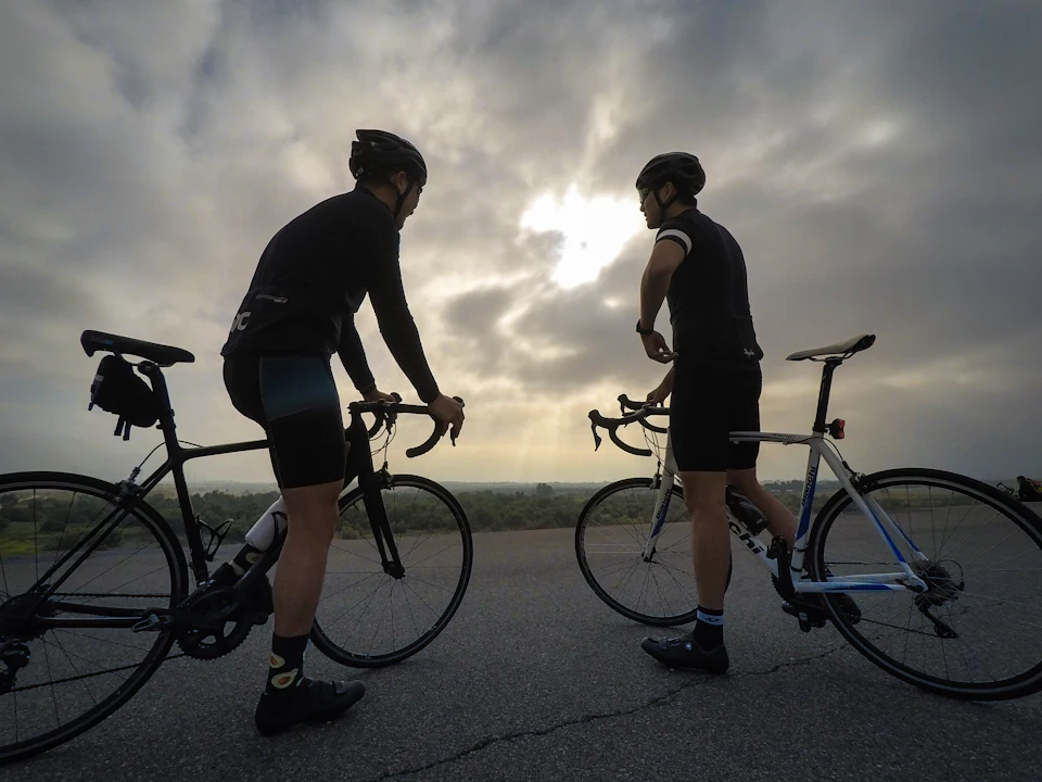 Two cyclists standing with their bikes, stopped for a chat under a cloudy sky