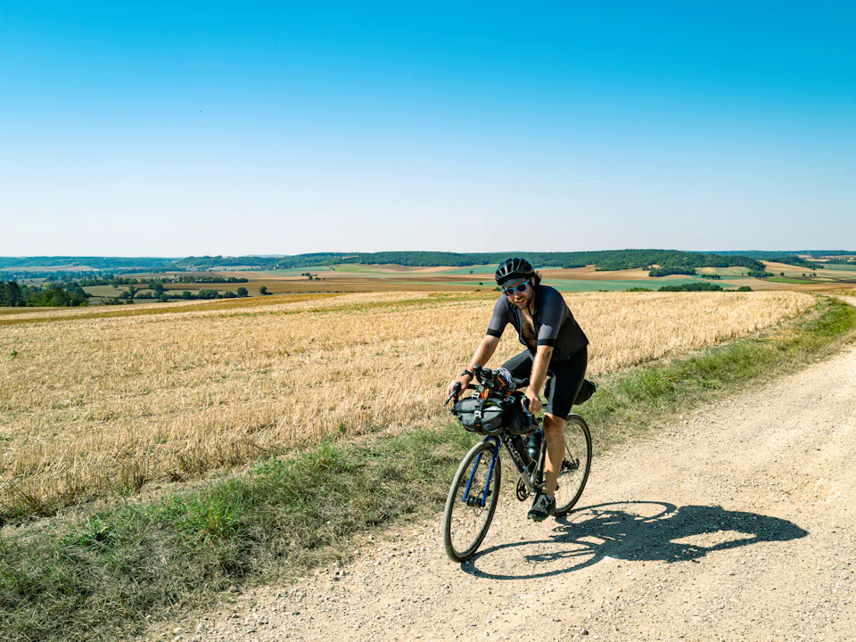 A cyclist with bike bags riding a gravel road past summer fields
