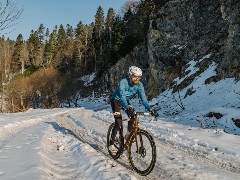 A cyclist riding a snowy road through a forest