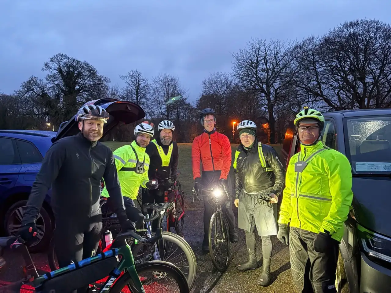 Six riders in hi-vis with lights on, gathered with their bikes in a car park at dawn before the Birr 200