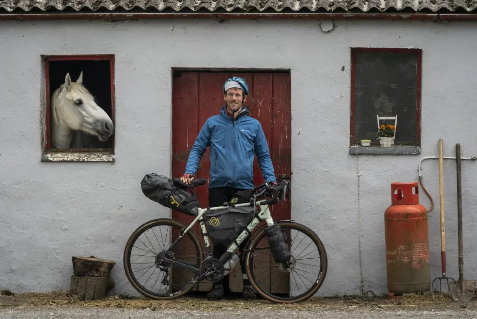 Peter with his bike outside a farmhouse on the TransAtlanticWay, a horse looking out the window