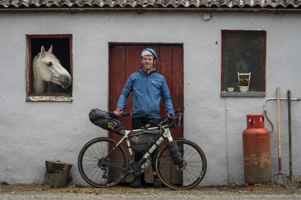 Peter with his bike outside a farmhouse on the TransAtlanticWay, a horse looking out the window